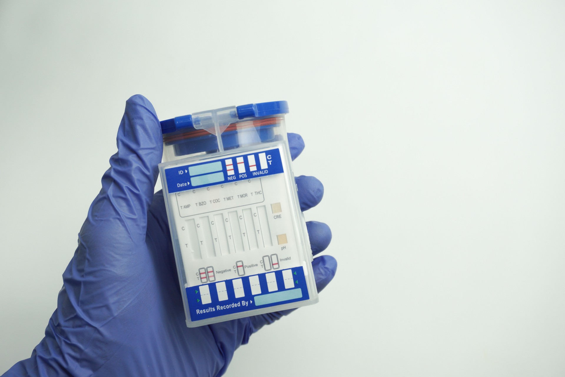 Hand in blue glove holding an empty container for analysis. Drug test concept. Isolated on white background.